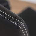 image rapprochée d'un ensemble de chaises moderne en cuir noir avec coutures blanches et pieds en bois sombre.