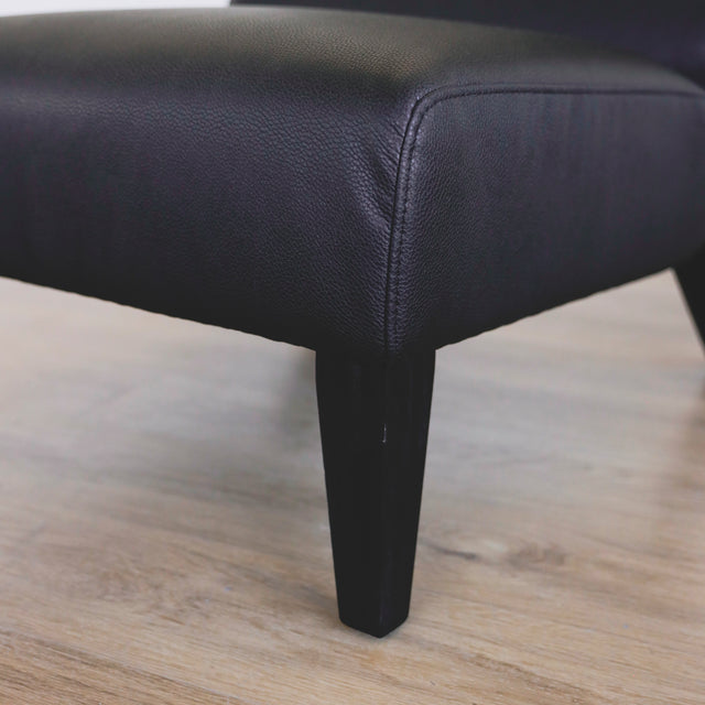 image rapprochée d'un Fauteuil moderne en cuir noir avec dossier capitonne et pieds en bois fonce.