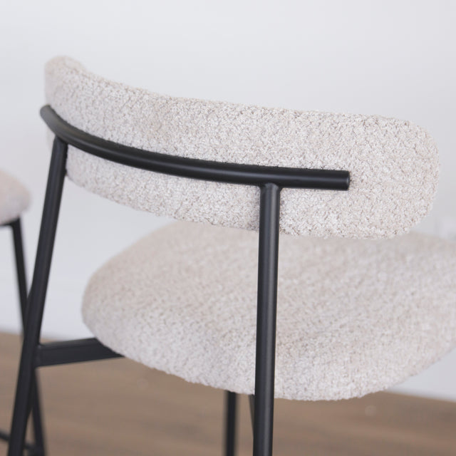 Image rapprochée de l'arrière d'une paire de tabourets en tissu crème bouclé avec pieds metalliques noirs.