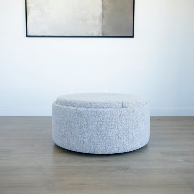 Pouf rond en tissu bouclé gris  avec plateau noir amovible sur sol en bois clair.