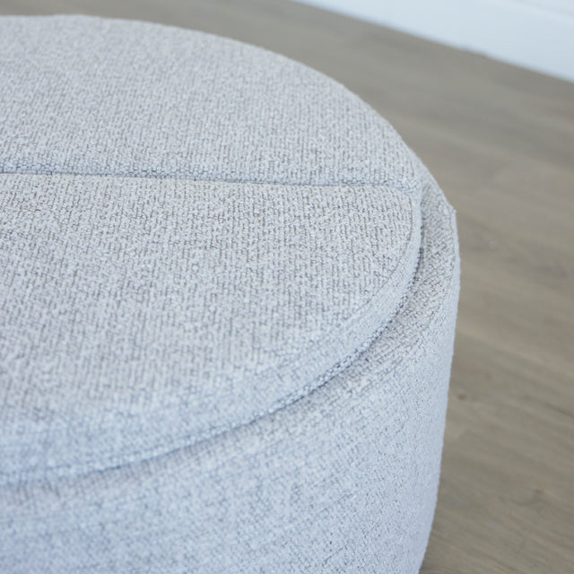 Image rapprochée d'un Pouf rond en tissu bouclé gris  avec plateau noir amovible sur sol en bois clair.