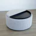 Pouf rond en tissu bouclé gris  avec plateau noir amovible sur sol en bois clair.