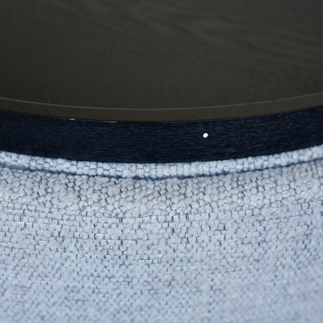 Image rapprochée d'un Pouf rond en tissu bouclé gris  avec plateau noir amovible sur sol en bois clair.