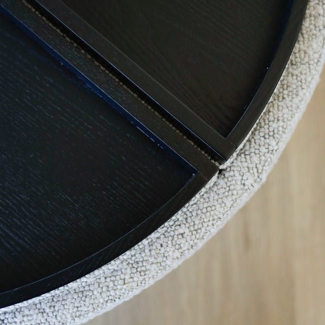 Image rapprochée d'un Pouf rond en tissu bouclé gris  avec plateau noir amovible sur sol en bois clair.