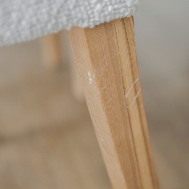 image rapprochée d'un ensemble de chaises modernes en tissu bouclé ivoire avec pieds en bois pâle avec défaut d'un accroc sur une patte.