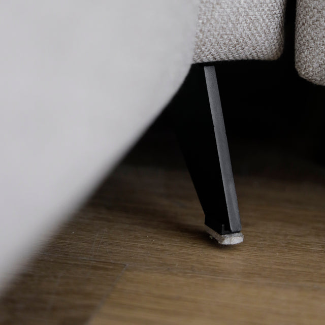 Image rapprochée de la patte d'un modulaire inclinable moderne en tissu gris clair avec pieds metalliques noirs sur parquet clair.