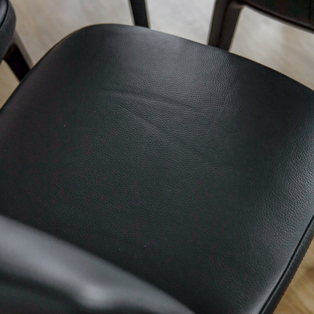 image rapprochée d'un ensemble de six chaises modernes en cuir noir avec pieds en bois noir sur parquet clair.