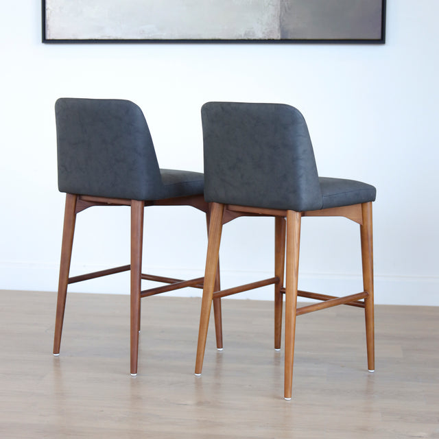 Deux tabourets de comptoir en cuir végane noir avec pieds en bois noyer, style moderne pour cuisine ou salon.