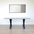 Table rectangulaire en beton avec pieds en metal noir en X, style industriel moderne.