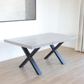 Table rectangulaire en beton avec pieds en metal noir en X, style industriel moderne.