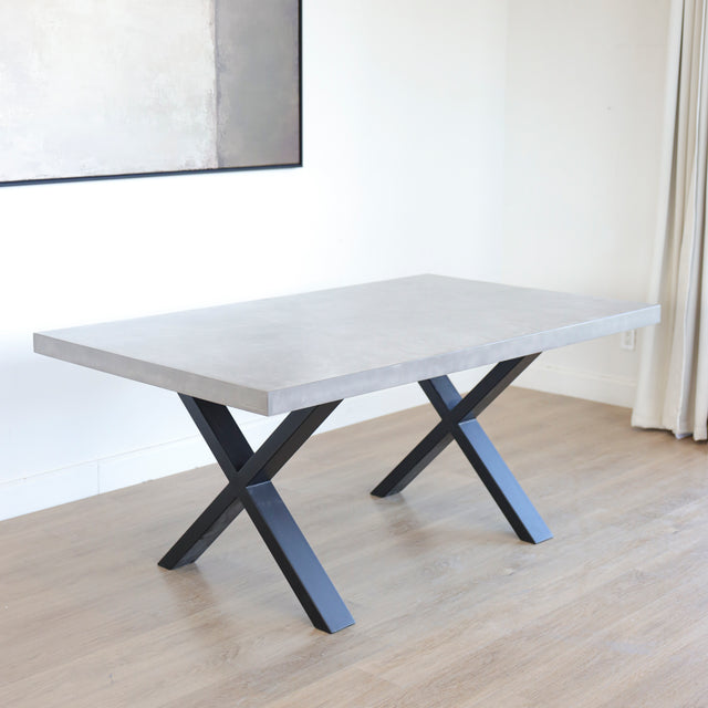 Table rectangulaire en beton avec pieds en metal noir en X, style industriel moderne.