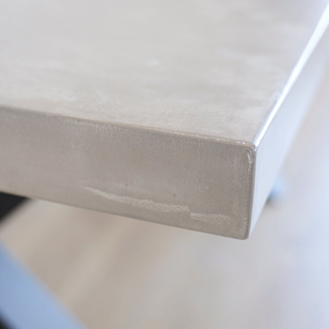 Image rapprochée table rectangulaire en beton avec pieds en metal noir en X, style industriel moderne.