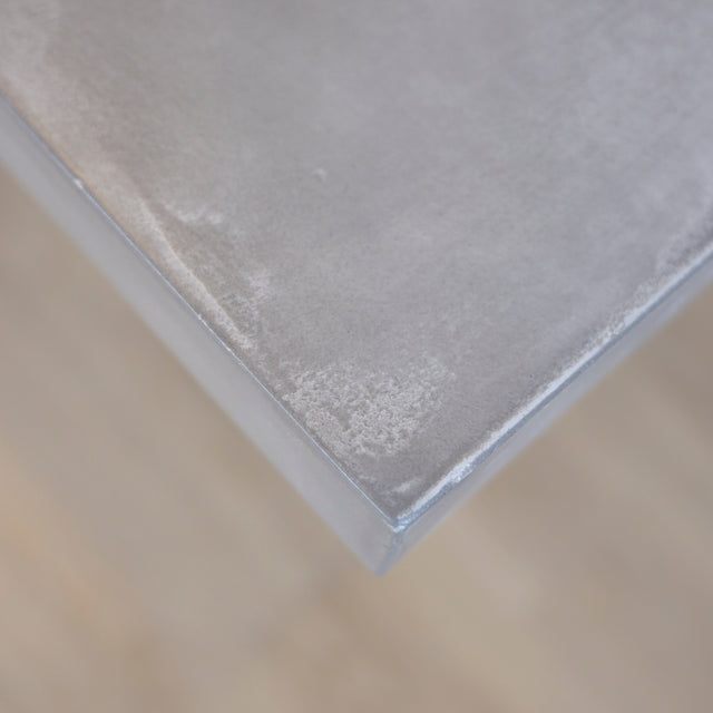 Image rapprochée table rectangulaire en beton avec pieds en metal noir en X, style industriel moderne.