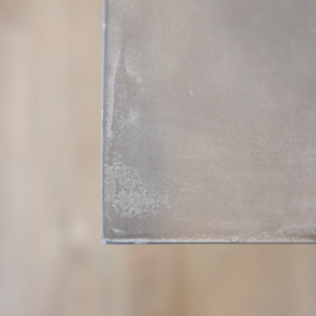 Image rapprochée table rectangulaire en beton avec pieds en metal noir en X, style industriel moderne.