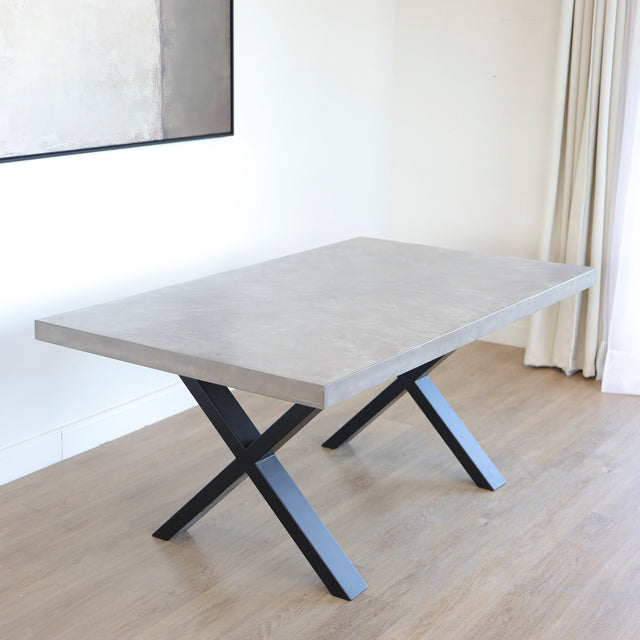 Table rectangulaire en beton avec pieds en metal noir en X, style industriel moderne.