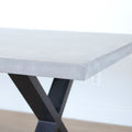 Image rapprochée table rectangulaire en beton avec pieds en metal noir en X, style industriel moderne.