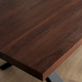 Image rapprochée d'une table rectangulaire en bois fonce avec pieds en metal noir en X, style industriel contemporain.