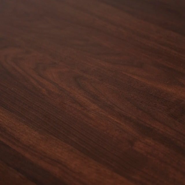 Image rapprochée d'une table rectangulaire en bois fonce avec pieds en metal noir en X, style industriel contemporain.