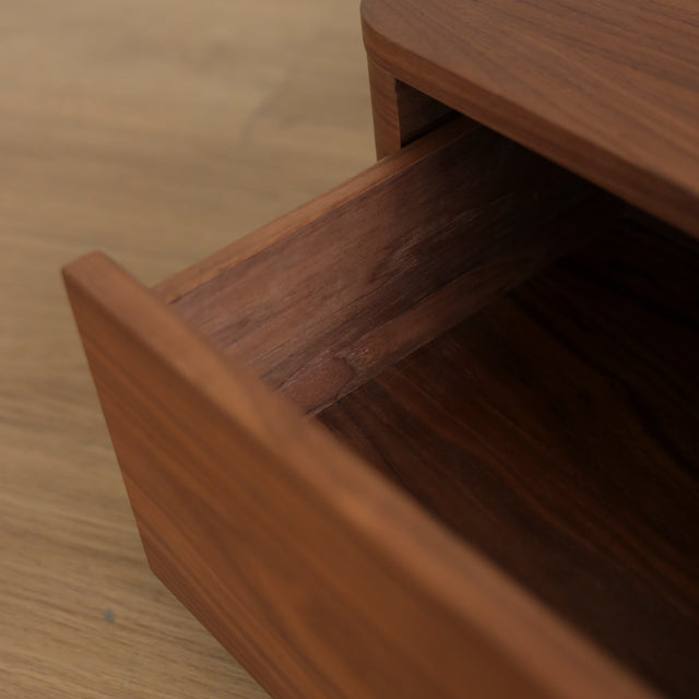 Image rapprochée d'une table de chevet moderne en bois noyer avec coins arrondis et tiroir integre.