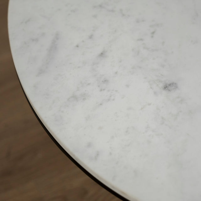 Image rapprochée d'une Table basse ronde avec plateau en marbre blanc et structure en metal noir, style moderne et minimaliste.
