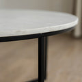 Image rapprochée d'une Table basse ronde avec plateau en marbre blanc et structure en metal noir, style moderne et minimaliste.