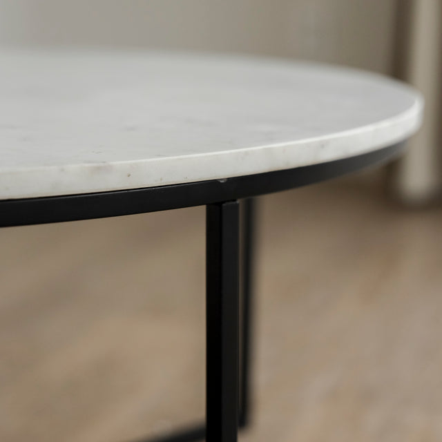 Image rapprochée d'une Table basse ronde avec plateau en marbre blanc et structure en metal noir, style moderne et minimaliste.