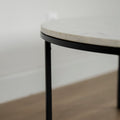 Image rapprochée d'une Table basse ronde avec plateau en marbre blanc et structure en metal noir, style moderne et minimaliste.