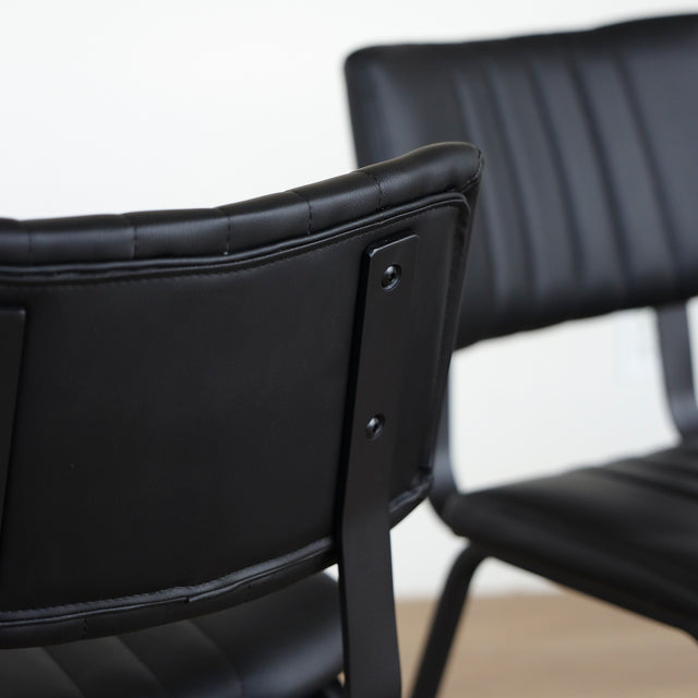 Deux chaises noires en simili cuir avec structure en metal, design industriel moderne.