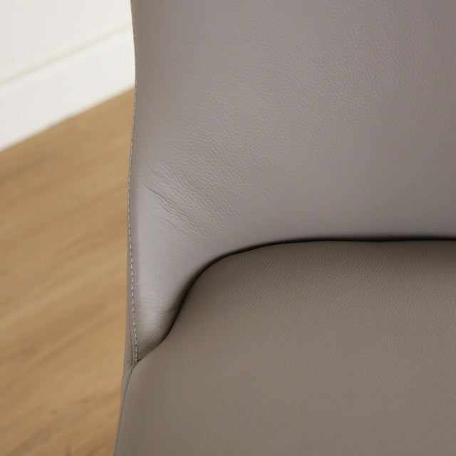 Image rapprochée d'une Chaise moderne en cuir gris avec assise rembourree et pieds en bois.