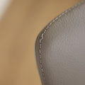 Image rapprochée d'une Chaise moderne en cuir gris avec assise rembourree et pieds en bois.