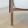 Fauteuil moderne en tissu bouclé ivoire avec structure en bois, idéal pour salon contemporain lumineux.