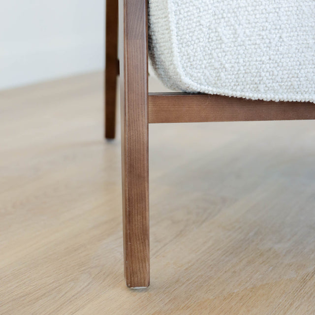 Fauteuil moderne en tissu bouclé ivoire avec structure en bois, idéal pour salon contemporain lumineux.