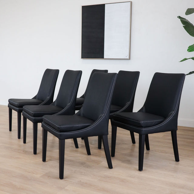 Lot de 4 chaises de cuisine, cuir végane noir, pattes noires, avec coutures contrastantes dans un décor moderne et lumineux. 