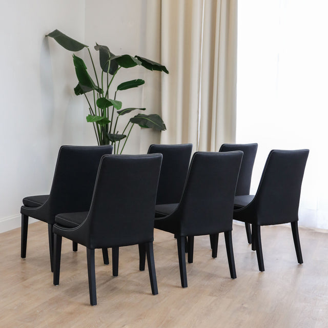 Lot de 4 chaises de cuisine, cuir végane noir, pattes noires, avec coutures contrastantes dans un décor moderne et lumineux. 