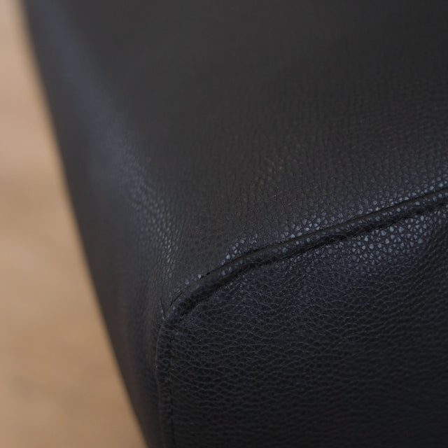 Fauteuil  en cuir végane noir avec dossier matelassé et pieds inclinés, style moderne pour salon. 