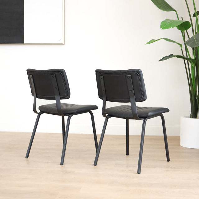 Deux chaises de salle à manger en cuir végane noir,  piètement en métal, design moderne, présentées dans un intérieur minimaliste.
