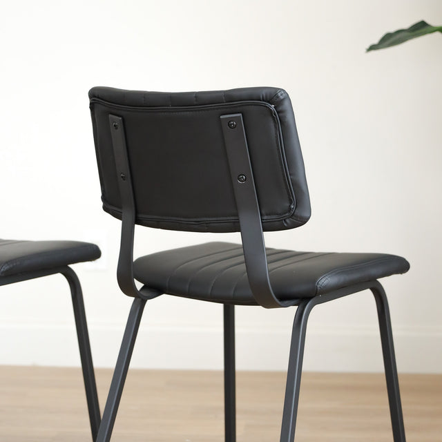 Deux chaises de salle à manger en cuir végane noir,  piètement en métal, design moderne, présentées dans un intérieur minimaliste.