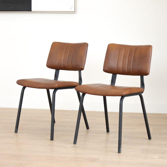 Deux chaises de salle à manger en cuir végane cognac, piètement métal noir, style industriel moderne.
