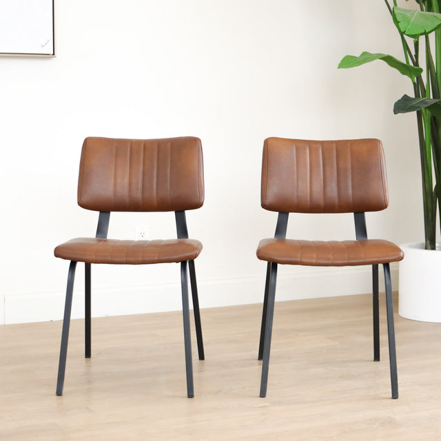 Deux chaises de salle à manger en cuir végane cognac, piètement métal noir, style industriel moderne.