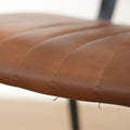 Deux chaises de salle à manger en cuir végane cognac, piètement métal noir, style industriel moderne.