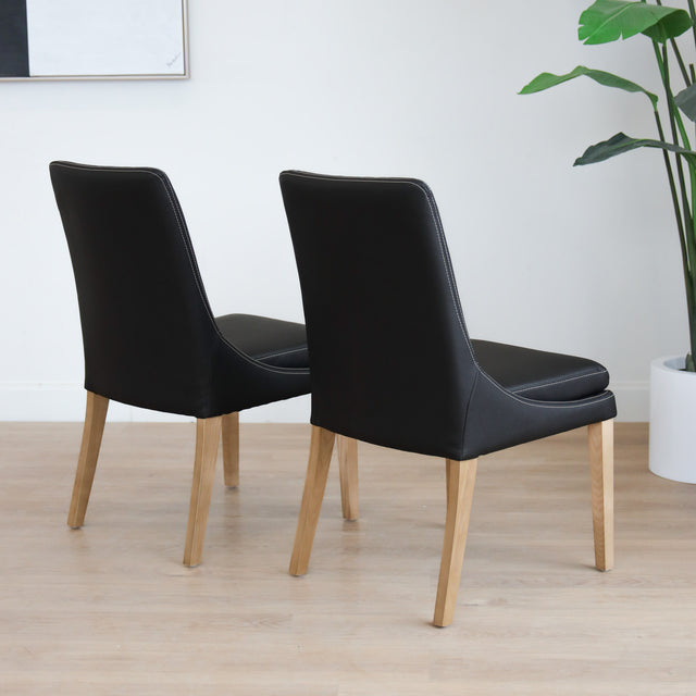 Lot de deux  chaises de salle à manger en cuir végane noir avec pattes en bois pâle, design moderne et élégant.
