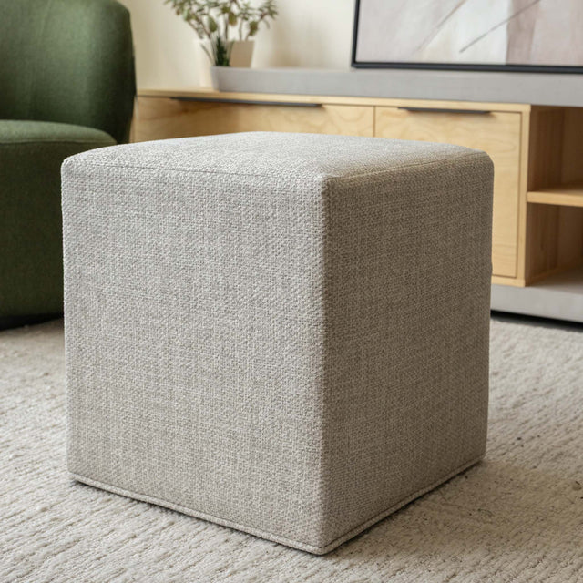 Ottoman cube beige en tissu texturé, idéal comme assise ou table d’appoint dans un salon moderne.