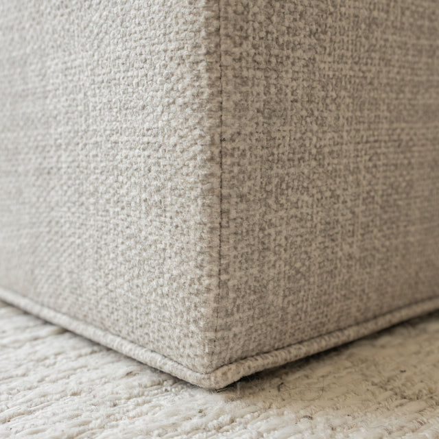 Ottoman cube beige en tissu texturé, idéal comme assise ou table d’appoint dans un salon moderne.