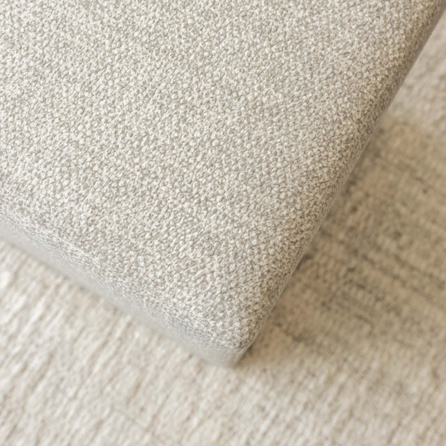 Ottoman cube beige en tissu texturé, idéal comme assise ou table d’appoint dans un salon moderne.