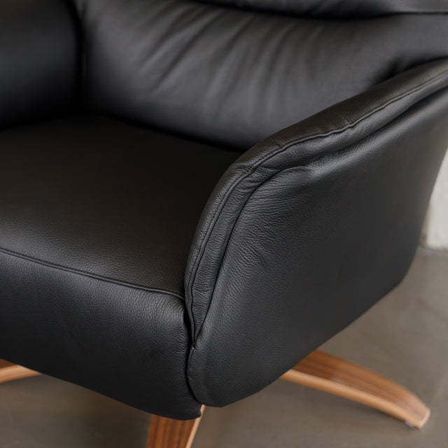 Fauteuil en cuir noir avec appui-tête et base bois pivotante, dans un intérieur chaleureux.