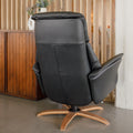 Fauteuil en cuir noir avec appui-tête et base bois pivotante, dans un intérieur chaleureux.