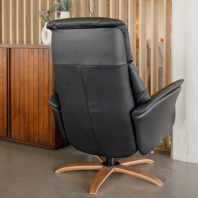 Fauteuil en cuir noir avec appui-tête et base bois pivotante, dans un intérieur chaleureux.