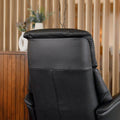 Fauteuil en cuir noir avec appui-tête et base bois pivotante, dans un intérieur chaleureux.