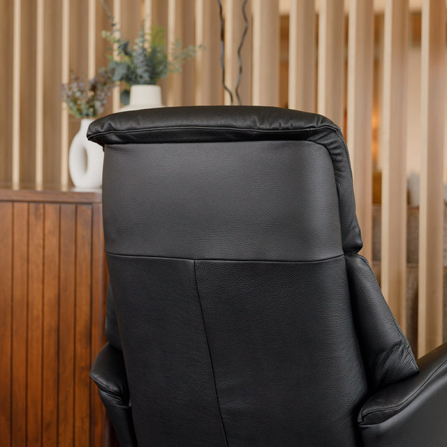 Fauteuil en cuir noir avec appui-tête et base bois pivotante, dans un intérieur chaleureux.