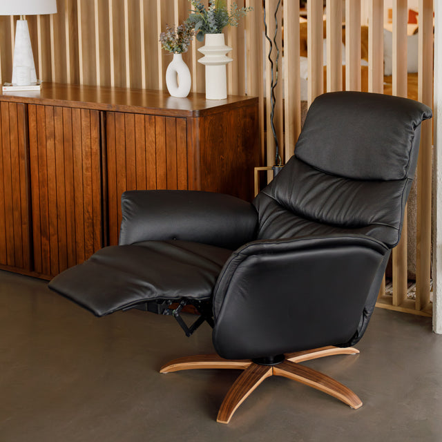 Fauteuil en cuir noir avec appui-tête et base bois pivotante, dans un intérieur chaleureux.